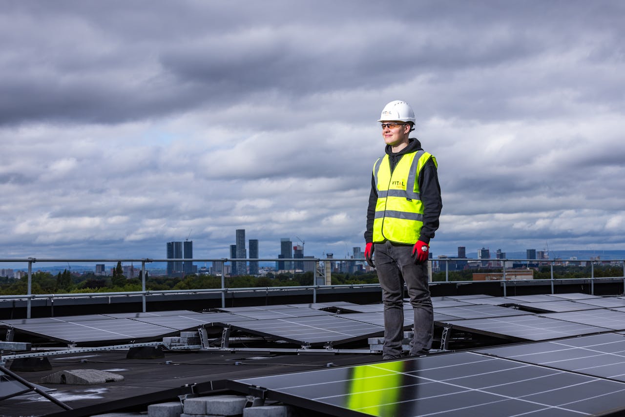 why-choose-us Engineer standing on rooftop inspecting solar panels with city skyline in background.