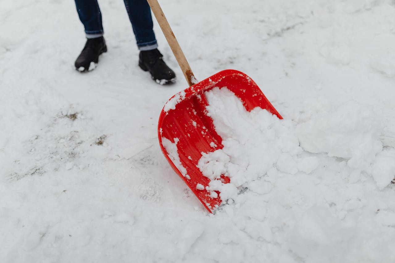 portfolio-03 Red shovel clearing snow outdoors during winter season.